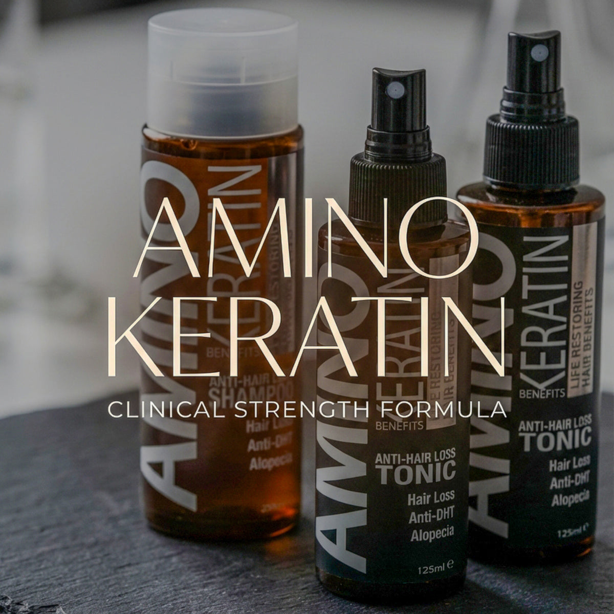 Three amber bottles of Amino Keratin hair care products, including shampoo, tonic, and a spray, arranged on a dark surface with large overlaid text reading 'AMINO KERATIN CLINICAL STRENGTH FORMULA'.